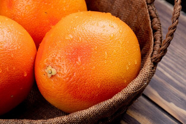 side view of fresh ripe oranges with water drops in a wicker basket on wooden surface