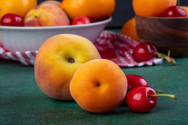 Side view of fresh ripe peaches with red cherries on dark green