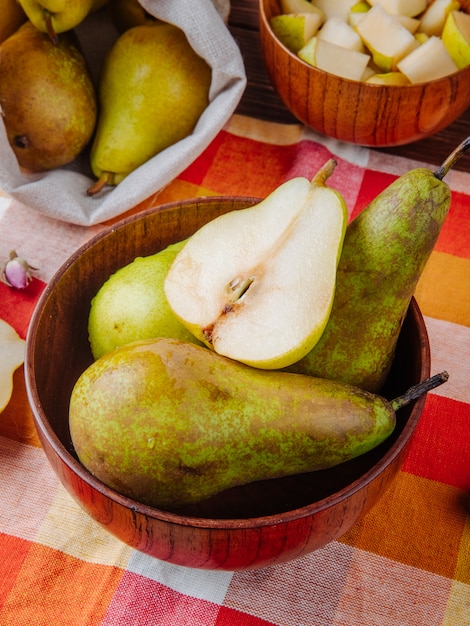 Foto gratuita vista laterale delle pere mature fresche e una metà in una ciotola di legno sul fondo del plaid