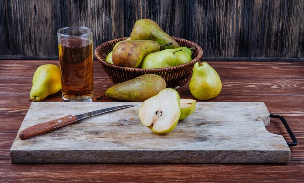 Side view of fresh ripe pears and halves on a wooden cutting board with kitchen knife on rustic background