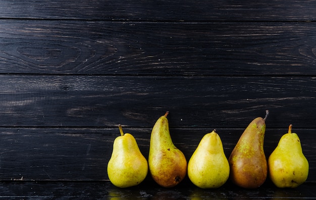 Side view of fresh ripe pears in a line on black wooden background with copy space