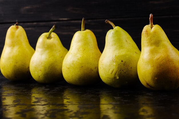 Side view of fresh ripe pears in a line on black wooden background