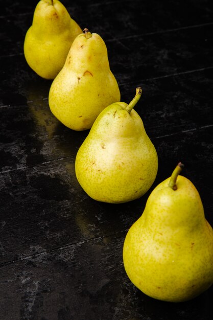 Side view of fresh ripe pears in a line on black wooden background