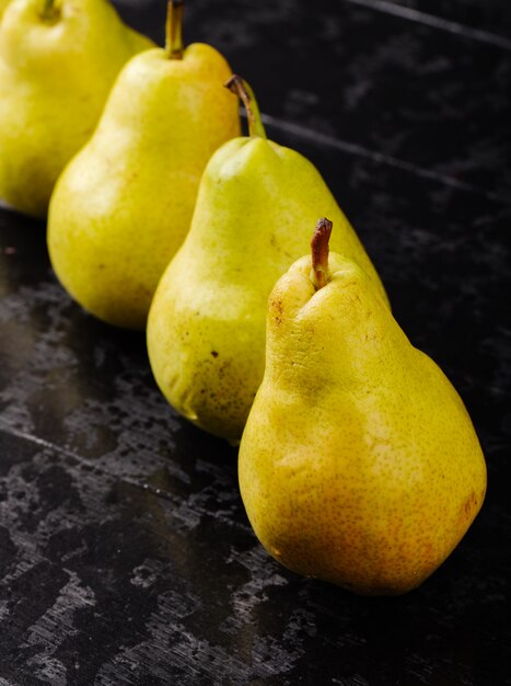 Side view of fresh ripe pears in a line on black wooden background