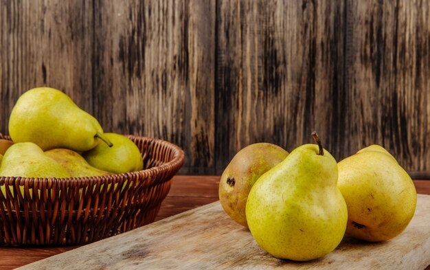 Side view of fresh ripe pears in a wicker basket and on a cutting board on a wooden background