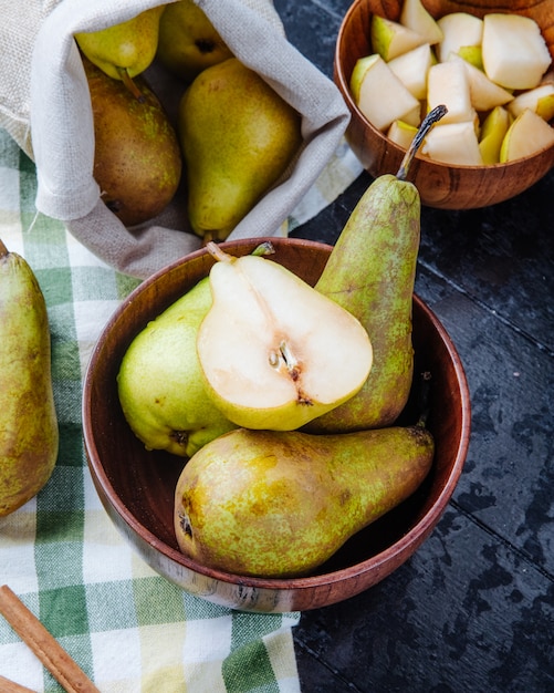 Side view of fresh ripe pears in a wooden bowl on black background