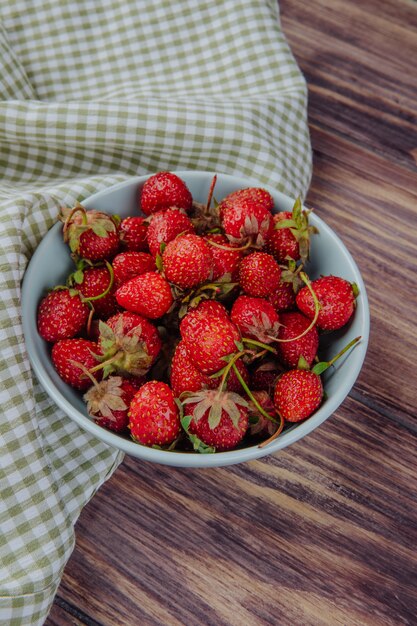 Side view of fresh ripe strawberries in a bowl on wood rustic