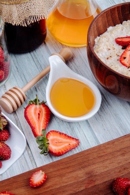 Side view of fresh ripe strawberries on a wood board with honey and oatmeal porridge in wood bowl on rustic_