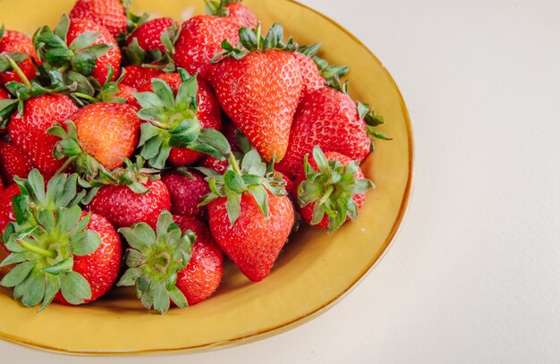 side view of fresh ripe strawberries in a yellow plate on white surface