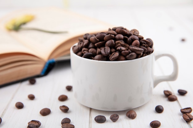 白い木製の背景の上の白いカップに新鮮な焙煎コーヒー豆の側面図