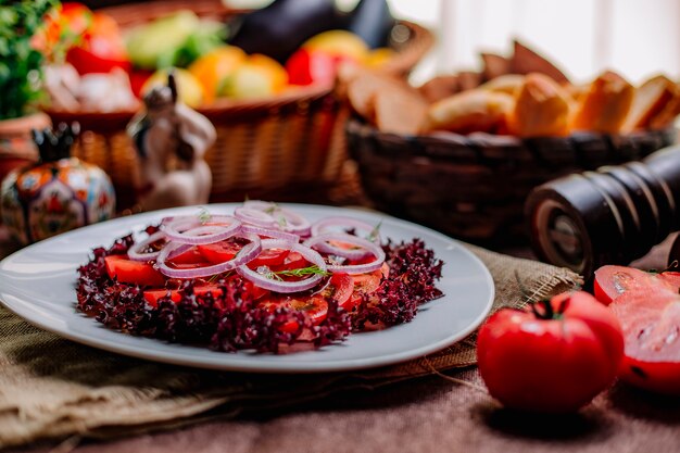 白い皿にスライスしたトマトの赤いレタスとタマネギのフレッシュサラダの側面図