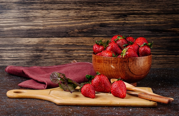 Side view fresh strawberry with basil and board on wooden background