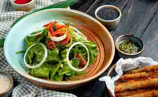 Free photo side view of fresh vegetable salad in a plate served with soy sauce and black seeds on wooden table