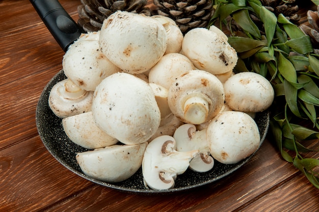 side view of fresh white mushrooms on a frying pan on wooden surface