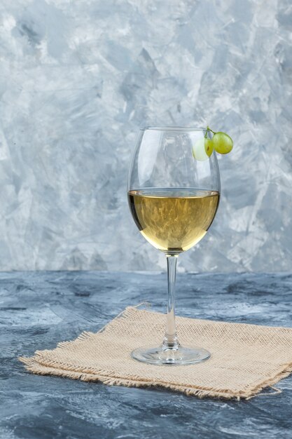 Вид сбоку свежее вино в стекле с виноградом на штукатурке и фоне мешка. вертикальный