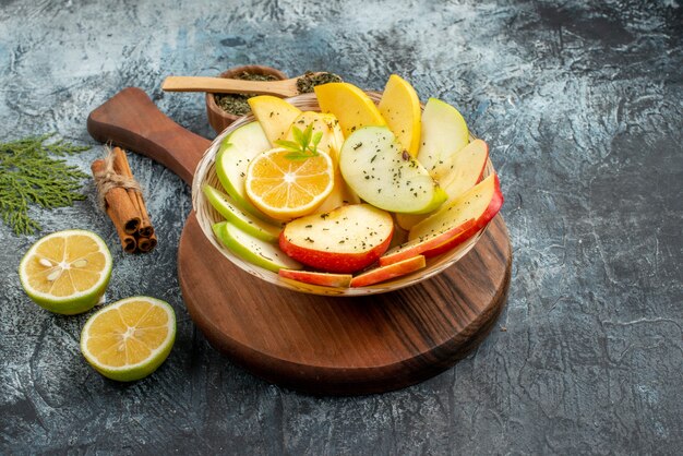 Side view of fresh yellow green red apple slices on a white plate with lemon on a wooden cutting board cinnamon limes on gray background