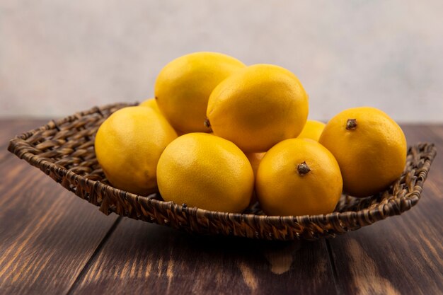 Вид сбоку свежих желтых лимонов на плетеном подносе на деревянной поверхности
