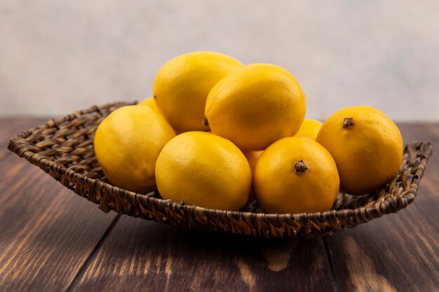 Side view of fresh yellow lemons on a wicker tray on a wooden surface