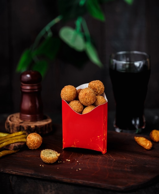 Side view of fried breaded cheese ball in cardboard bag on wooden table