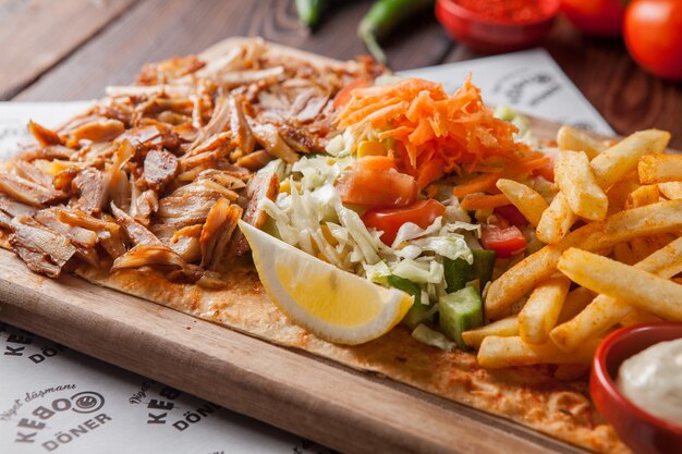 Side view fried chicken pieces with lemon and french fries and salad in wood plate