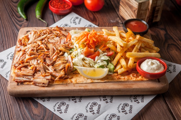 Side view fried chicken pieces with lemon and french fries and sauce in wood plate