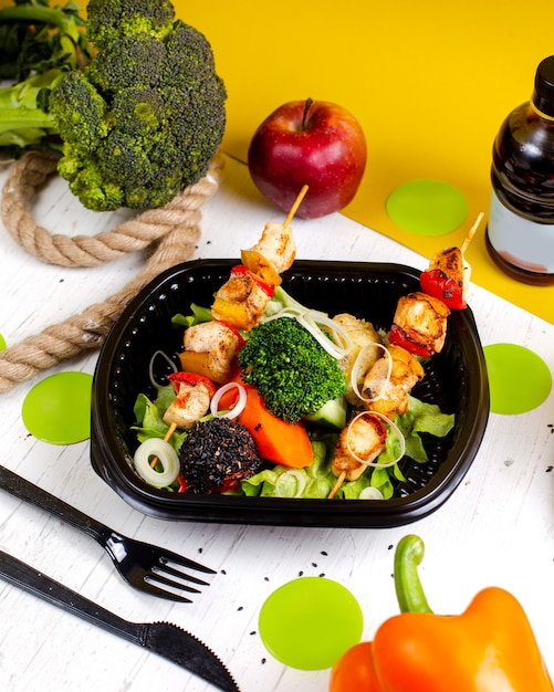 Free photo side view of fried chicken on skewers with fresh vegetables broccoli and onions in a delivery box