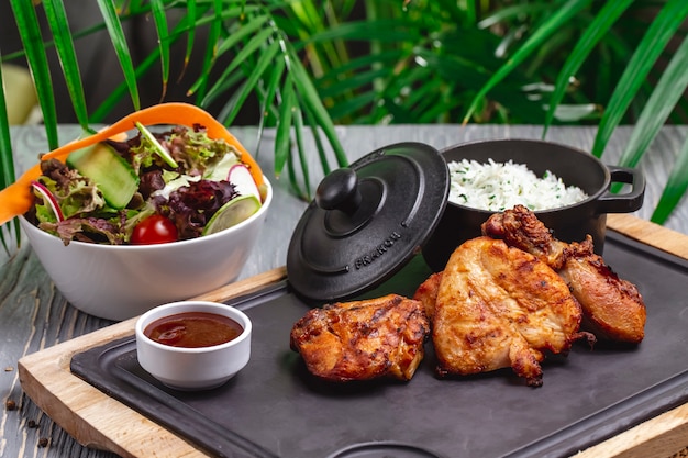 Free photo side view fried chicken with boiled rice in a pan and vegetable salad with sauce