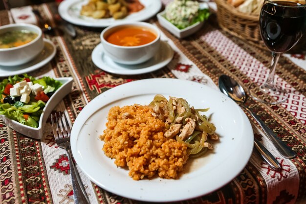 Side view fried chicken with onions bulgur and vegetable salad with soup on the table