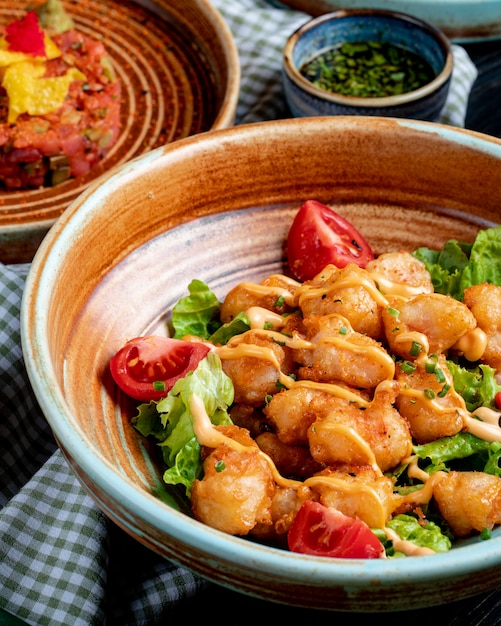 Side view of fried chicken with tomatoes and sauce on lettuce on a plate on rustic