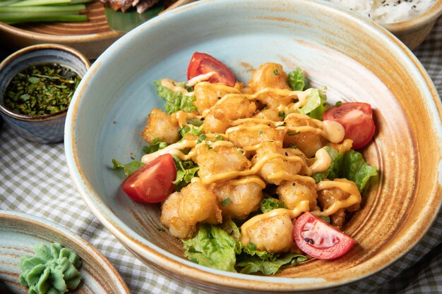 Side view of fried chicken with tomatoes and sauce on lettuce on a plate on rustic