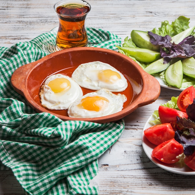 Free Photo side view fried eggs with chopped tomatoes and chopped cucumbers and glass of tea in clay plate