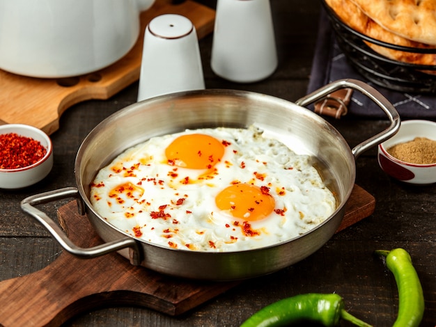 Side view of fried eggs with red spices in a pan on wooden board