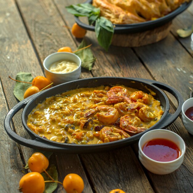 Side view of fried eggs with shrimps and vegetables in a pan served with sauces