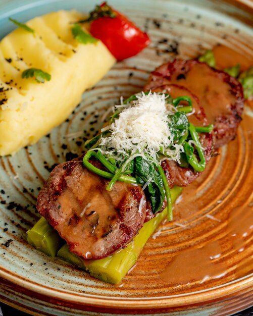 Side view fried meat on asparagus with mashed potatoes and herbs in a plate