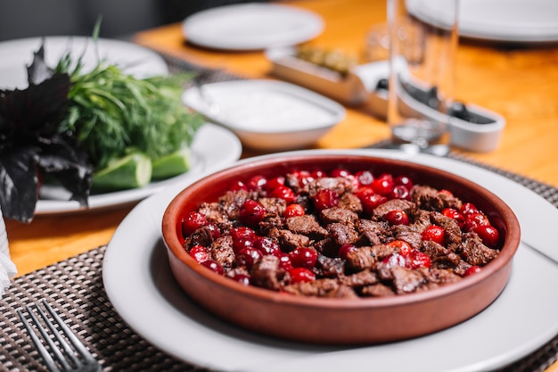 Side view of fried pieces of meat with cherries in a clay bowl