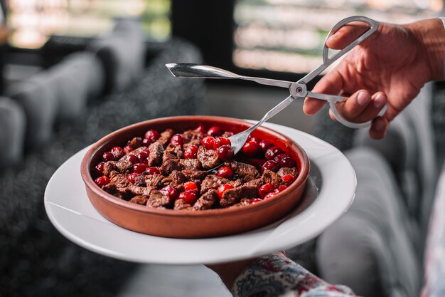 Side view of fried pieces of meat with cherries in a clay bowl