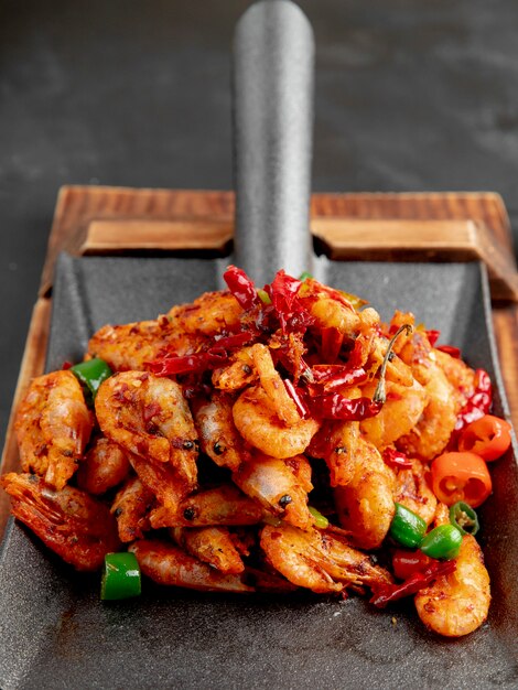 Side view of fried shrimps with red and green peppers on a wooden cutting board