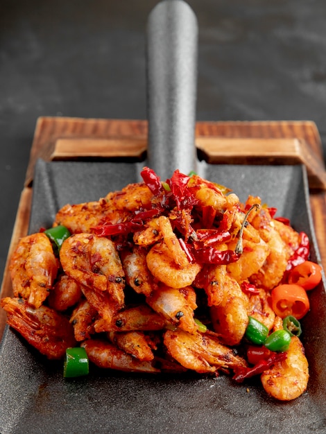 Side view of fried shrimps with red and green peppers on a wooden cutting board