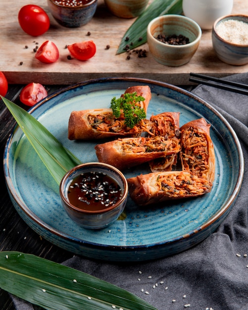 Side view of fried spring rolls with chicken and vegetables served with soy sauce on a plate on black