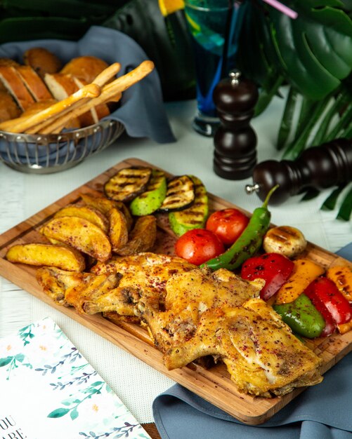 Вид сбоку жареного табака курица с картофелем и овощами гриль на деревянной доске
