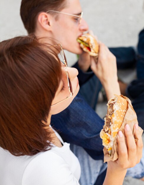 Друзья едят гамбургеры на открытом воздухе, вид сбоку