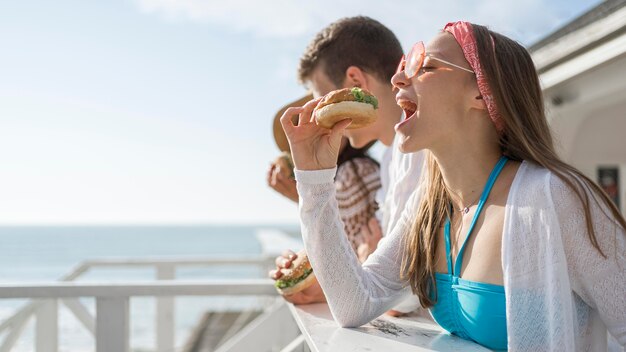 Side view of friends outdoors eating burgers together