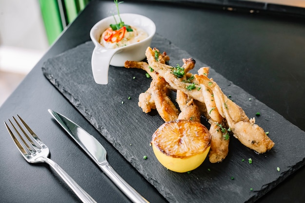 Side view frog legs in batter with sauce and lemon on a tray