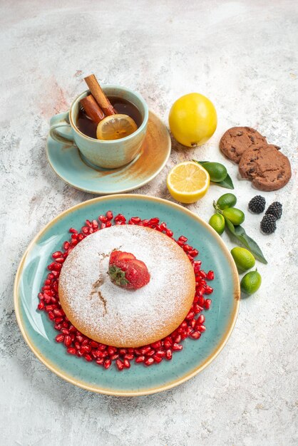 Вид сбоку на аппетитный торт чашка чая с лимонным шоколадным печеньем и торт с гранатом и клубникой