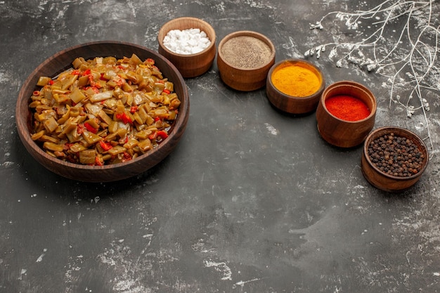 Free photo side view from afar appetizing dish five bowls of colorful spices next to the brown plate of the appetizing green beans and tomatoes