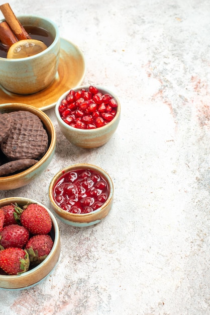 Vista laterale da lontano bacche in ciotole ciotole di frutti di bosco una tazza di tè con marmellata di cannella e biscotti