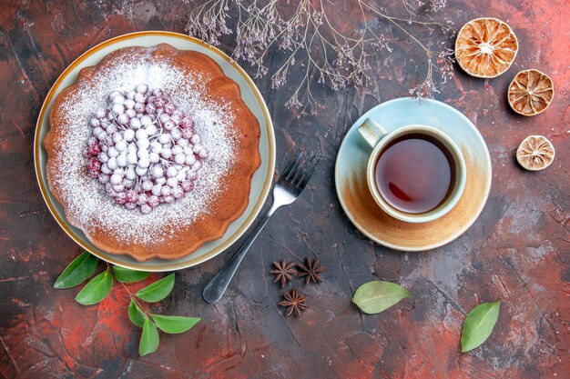 Side view from afar a cake a cake with berries leaves lemon fork a cup of tea star anise