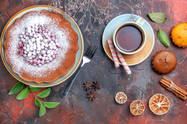 Side view from afar a cake a cake with berries leaves sweets cupcakes a cup of tea citrus fruits