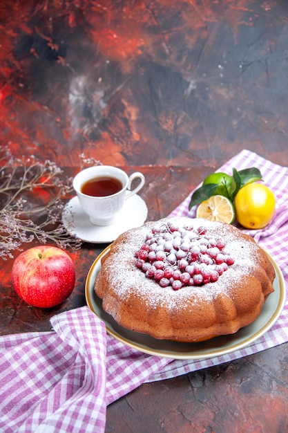 Side view from afar a cake a cake with red currants a cup of tea citrus fruits on the tablecloth