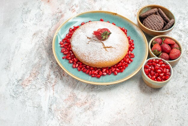 Free photo side view from afar cake cake with strawberries bowls of pomegranate cookies and berries